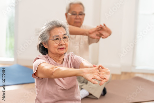 Senior Asian woman extends arms forward while seated cross-legged during gentle exercise in assisted living community, supporting shoulder mobility, flexibility, muscle recovery and healthy aging.