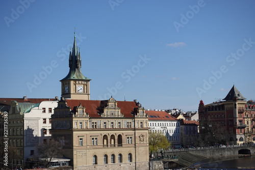 Panoramic cityscape of Prague displaying red terracotta rooftops, historic spires, and the Vltava River spanning across the urban horizon.