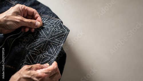 Artisan hands stitching Japanese Sashiko pattern on denim jacket in craft studio background banner.