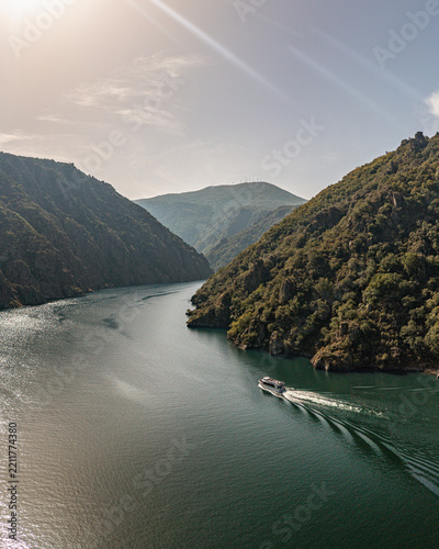 Aerial view of Ribeira Sacra with a boat cruising on the Sil River surrounded by steep, forested canyon walls under a bright sky Lugo, Orense, Spain.