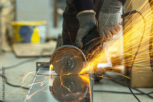 Close-up of a worker cutting a square galvanized ventilation pipe with an angle grinder