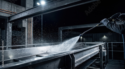 Industrial cleaning worker sprays water on stainless steel equipment, supporting food security solutions in dark processing facility