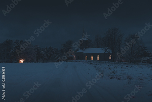 View of Vainupea Chapel illuminated at night in a snow-covered landscape with bare trees and a dark blue sky in Vainupea, Laane-Viru maakond, Estonia.