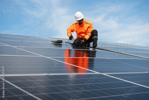 Technician installing solar panels on factory roof for green energy. A skilled technician in safety gear is working on a solar panel installation on rooftop.