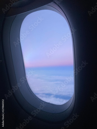 Airplane window view of a pastel pink and blue sky above soft clouds on sunset.
