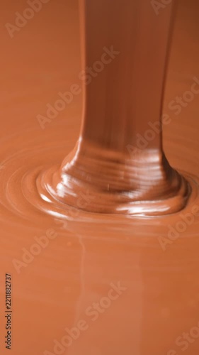 Thick stream of melted milk chocolate pouring into liquid chocolate pool.
