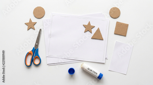 Cardboard shapes and paper sheets laid out with scissors and glue stick on white surface with sheets arranged clean cardboard cutouts development preparation with stationery