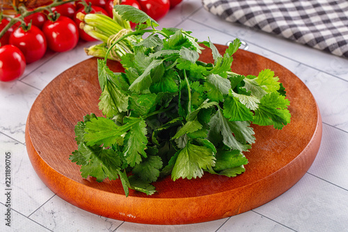 Fotografie Wooden cutting board with fresh green cilantro leaves and stems, cherry tomatoes
