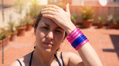 Woman shielding eyes from bright sunlight on a sunny outdoor terrace