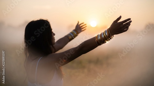 Woman stretching arms toward the sunrise in a misty outdoor field