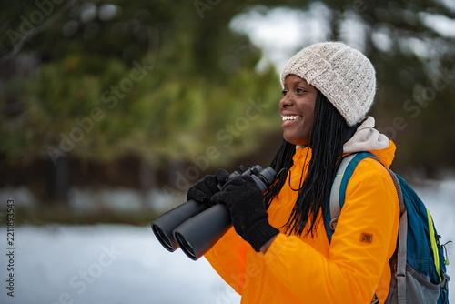 Happy woman enjoying winter birdwatching with binoculars and backpack