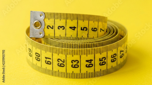 Yellow Measuring Tape Rolled Up on Bright Yellow Background Healthcare Diet Fitness Concept