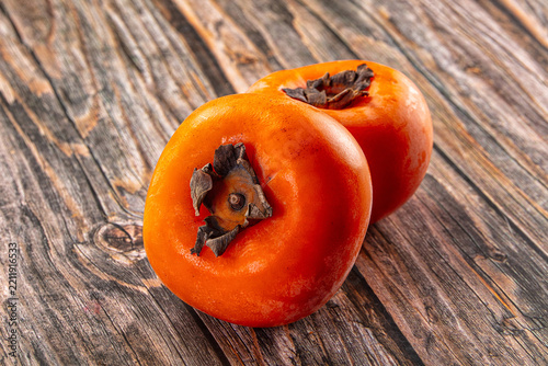Weathered wooden surface with two ripe orange persimmons showing dried calyxes, autumn fruit still life