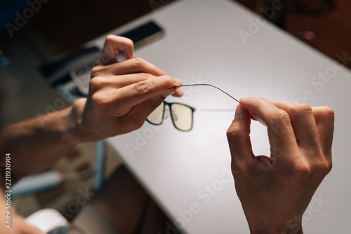 Person hands holding and bending eyewear temple arm. Concept of extreme flexibility and robust durability of lightweight frame material during resilience test, close-up, cropped shot