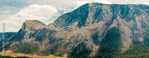 Dramatic Rocky Mountain Landscape with Forested Slopes and Cloudy Sky