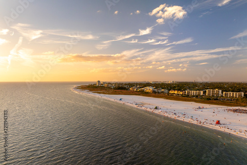 Crowded Siesta Key beach in Sarasota with clear blue water and soft sand, tourists swimming and relaxing under warm Florida sun at sunset.