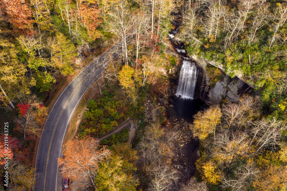 Obraz premium Looking Glass Falls and Forest Heritage Scenic Byway from above during fall season. Scenic mountain road carries passing cars beside waterfall and observation platform in Pisgah National Forest.