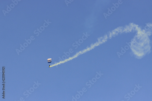 Skydiver with a white smoke trail descending in a spiral against a deep blue sky during an exhibition