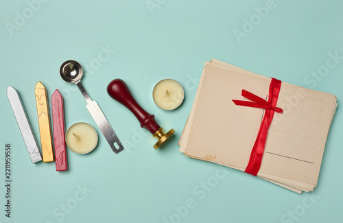 Vintage postcard, stack of letters with a red ribbon, candle, pencil, and wax seal on a turquoise background