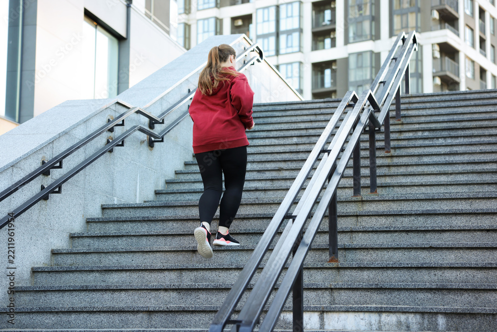 Fototapeta premium Overweight woman running up stairs on city street, back view. Space for text