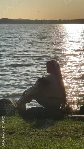 Silhouette Of Long Haired Woman Sitting On Lake Bank At Sunset Video