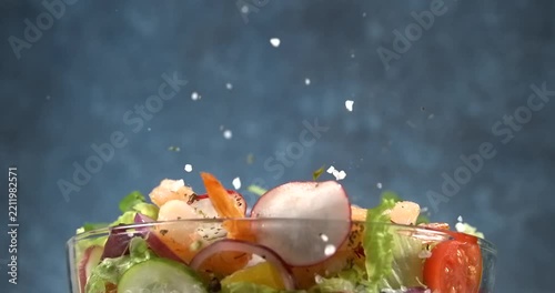 Shrimp falling onto fresh vegetable salad with avocado in slow motion
