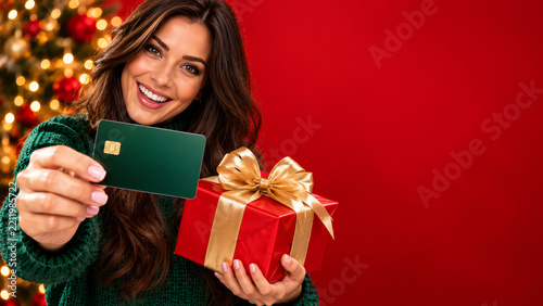 Woman holding bank card and Christmas gift for holiday shopping sale with festive tree and red banner copy space online.