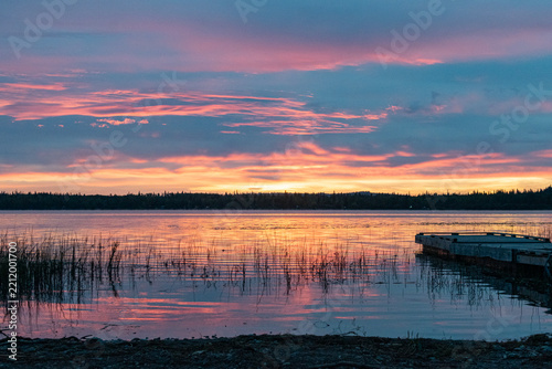 Colorful sunrise over reflective lake with fishing dock