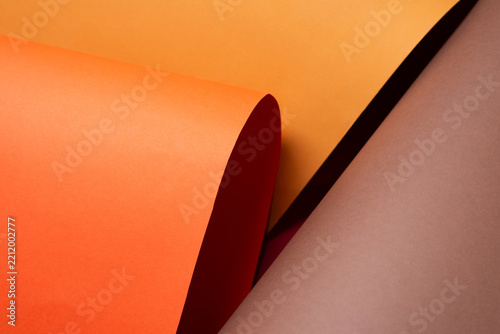 Close up of curled orange paper overlapping yellow and brown sheets, with a glimpse of red beneath