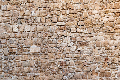 Background with an ancient stone wall with irregularly shaped rocks and rough texture, showing weathered and aged construction details.