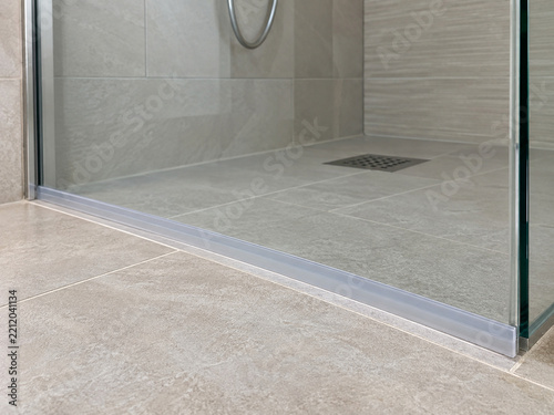 Clear shower threshold strip along tiled floor beside a glass enclosure