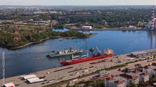 High-angle aerial view of a military vessel towing another ship through Halifax Harbour, passing under a bridge in Halifax, Nova Scotia, during the early morning hours.
