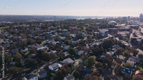 High-angle drone shot of Halifax, Nova Scotia, showing the city skyline, blue harbour waters, maritime traffic, and major urban roads with cars, delivery vehicles, and heavy trucks moving through 