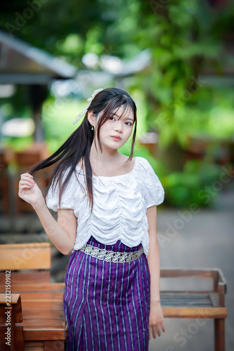 a beautiful Asian woman in traditional Thai attire posing gracefully outdoors.