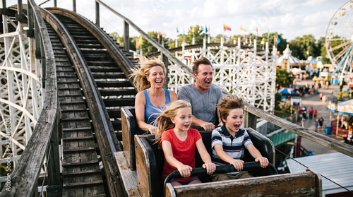 Happy family enjoying thrilling wooden roller coaster ride at an amusement park.