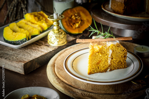 Homemade Halloween pumpkin spice cake with white icing glaze and cinnamon sticks on a rustic table with candles, dark spooky ambiance, and autumn decor for festive seasonal baking concept.