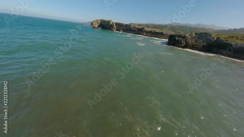 Dynamic FPV drone shot flying through a natural stone archway and over turquoise ocean waves crashing against the rugged coastline of Playa de la Canalona.