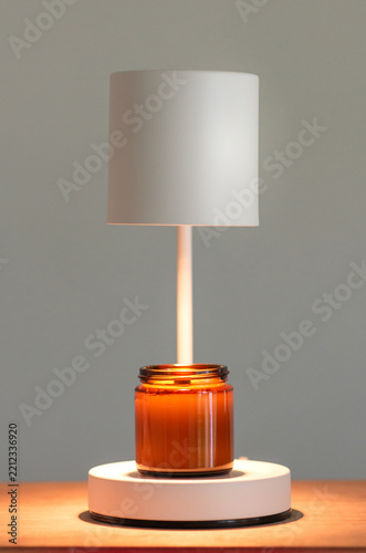 Scented candle in an amber glass jar under a white warmer lamp on a wooden table