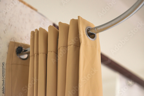 Beige fabric curtain hanging on a metal rod near a white wall.