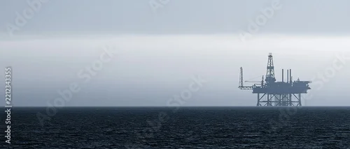 Panel kuchenny z motywem Silhouette of an offshore oil rig platform stands in the dark, choppy ocean under a hazy, overcast sky