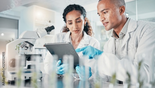 Two laboratory scientists working with digital tablet while conducting medical research and analyzing clinical data in a modern biotechnology facility