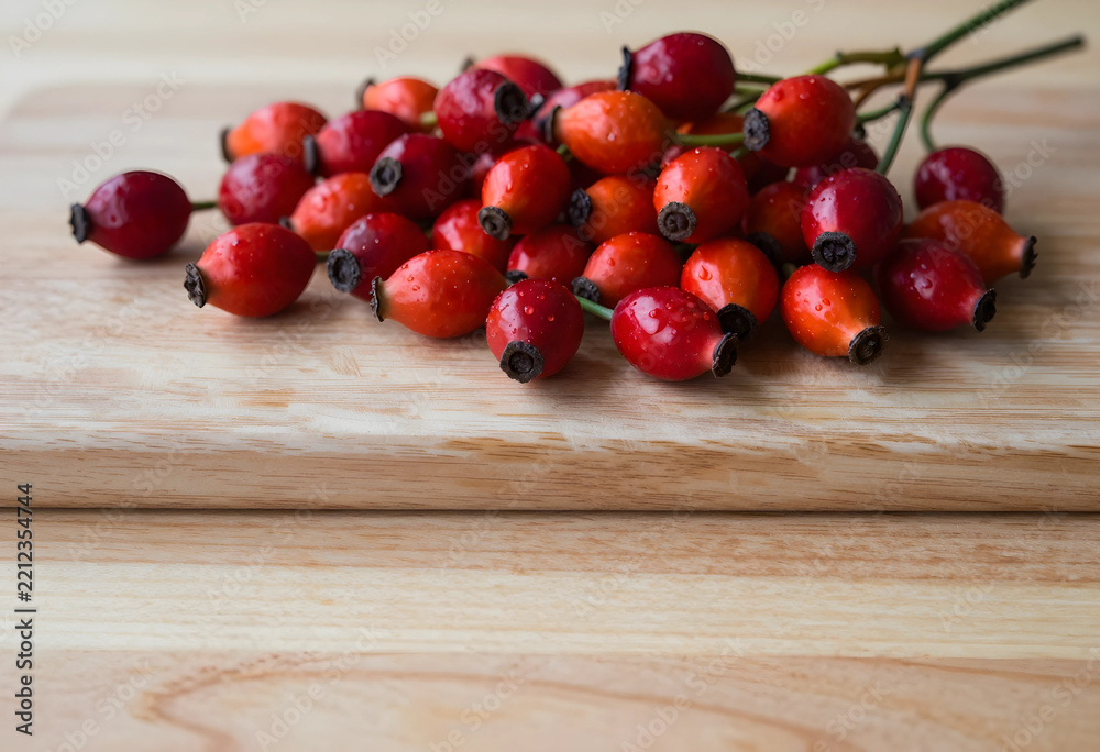Naklejka premium Rose hips for herbal medicine and nutrition, fresh red berries on a wooden cutting board for organic skincare and natural vitamin c supplement source