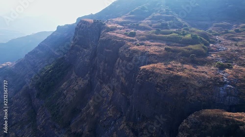 A drone video of majestic view of a rugged sunlit cliff side towering over deep mountain valleys