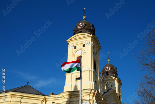Obraz na plátně Historic Reformed church in Debrecen, Hungary, photographed against a clear blue sky with the Hungarian national flag displayed on the facade