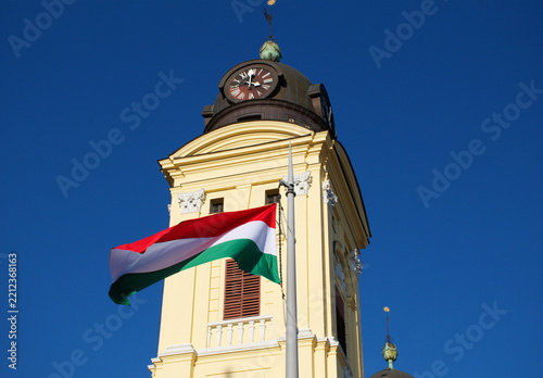 Obraz na plátně Historic Reformed church in Debrecen, Hungary, photographed against a clear blue sky with the Hungarian national flag displayed on the facade