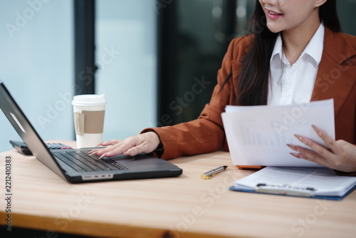 Businesswoman Typing on Laptop and Reviewing Documents at Office Desk