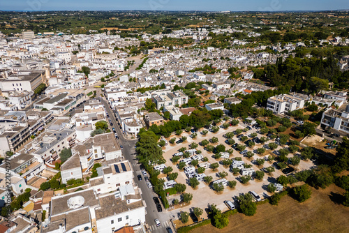 An aerial drone view shows a dedicated camperstop and RV parking area surrounded by olive trees in Alberobello, Italy. The facility sits conveniently right next to the historic UNESCO town filled with