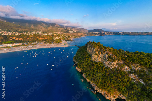 A breathtaking sunset aerial view captures Isola del Dino and the bay at Praia a Mare in Calabria, Italy. Boats navigate the deep blue waters along a sprawling beach, framed by dramatic coastal