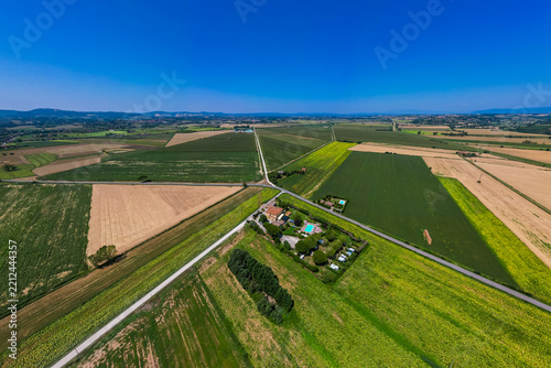 An aerial drone view reveals a charming Tuscan agriturismo nestled among vibrant sunflower fields and vast farmland. The property features a swimming pool and an organized camperstop for motorhomes in
