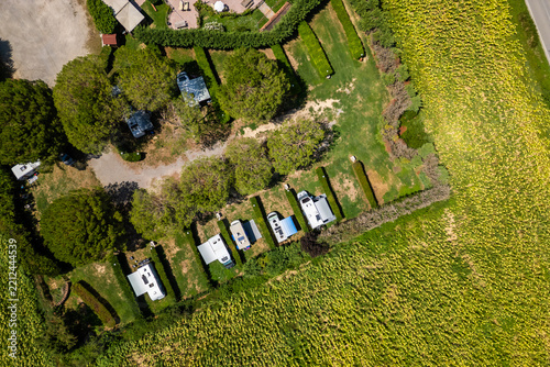 An aerial drone view reveals a charming Tuscan agriturismo nestled among vibrant sunflower fields and vast farmland. The property features a swimming pool and an organized camperstop for motorhomes in